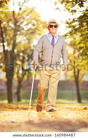 Full length portrait of a blind mature person holding a stick and walking in a park - stock photo
