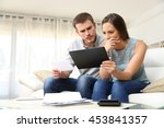 stock-photo-worried-couple-checking-bank-account-trouble-online-in-a-tablet-sitting-on-a-couch-in-the-living-453841357.jpg