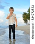 Small photo of Full growth portrait on a tropical beach: handsome slim boy - 8 years old - in wet clothes without shoos ankle-deep in water. He pondered and I put a hand to face. Beautiful sky on background