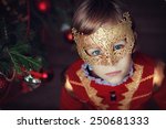 Small photo of A portrait of a little handsome boy in masquerade costume and a carnival mask against the decorated Christmas tree. Fancy-dress ball.