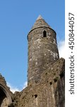 Small photo of A medieval round tower in Ireland set against a clear blue sky with ancient walls in the foreground.