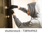 Small photo of Profile view of a man with a hoodie trying to pick a lock in a house and forcing his entry