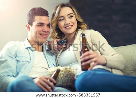 https://thumb10.shutterstock.com/display_pic_with_logo/1382728/583331557/stock-photo-happy-young-couple-sitting-on-the-sofa-at-home-with-popcorn-and-beer-watching-tv-they-are-583331557.jpg