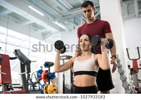 Waist Up Portrait Of Beautiful Young Woman Exercising With Dumbbells Sitting On Bench Helped By Personal Waist Up Portrait Of Beautiful Young Woman Exercising With Dumbbells Sitting On Bench Helped By Personal