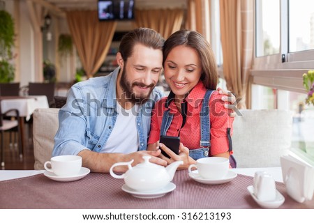 https://thumb10.shutterstock.com/display_pic_with_logo/2711341/316213193/stock-photo-cheerful-young-man-and-woman-are-sitting-and-embracing-in-cafeteria-the-girl-is-holding-a-mobile-316213193.jpg