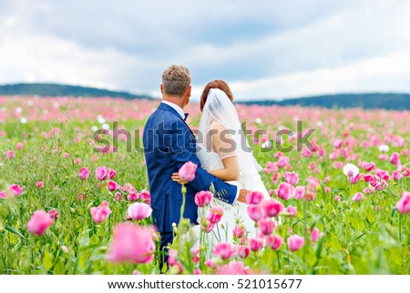 https://thumb10.shutterstock.com/display_pic_with_logo/658336/521015677/stock-photo-happy-wedding-couple-in-pink-poppy-field-beautiful-bride-young-woman-in-white-dress-and-oder-521015677.jpg