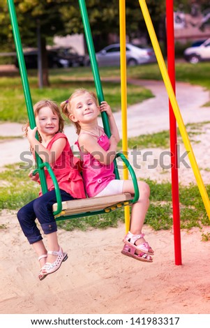 Two beautiful little girls on a swings outdoor in the playground at ...